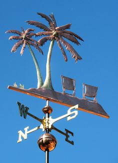 a weather vane with two chairs and a palm tree on it's top, against a blue sky