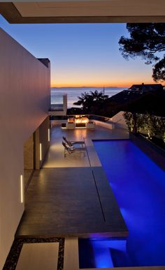 an outdoor dining area next to the ocean at night with lights on and bench in foreground