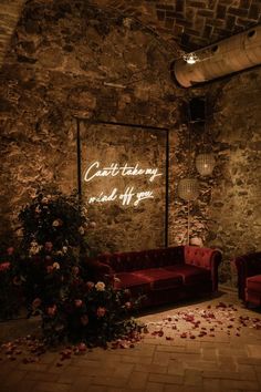 a red couch sitting in front of a stone wall next to a planter filled with flowers