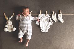 a baby is laying on the floor next to some clothes and a stuffed animal hanging from a line