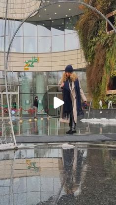 a woman is standing in front of a building with a fountain and umbrellas on the ground