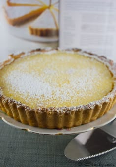 a pie with powdered sugar on top sits on a plate next to a fork