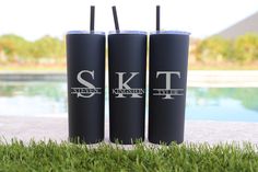 three black tumblers sitting next to each other on the grass near a swimming pool