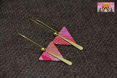 two triangle shaped earrings on top of a brown cloth with gold colored pins and hooks