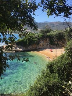 the beach is surrounded by trees and clear blue water, with people swimming in it