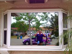 a man taking a selfie in the reflection of a window with a purple car behind him