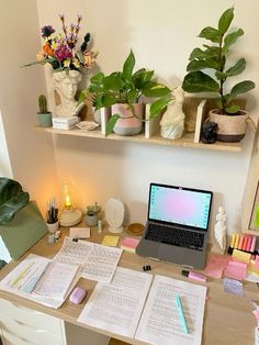 a laptop computer sitting on top of a wooden desk next to books and plants in vases