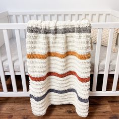 a crocheted blanket hanging from the side of a crib next to a white crib