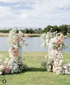 two tall vases with flowers are sitting in the grass near some water and trees