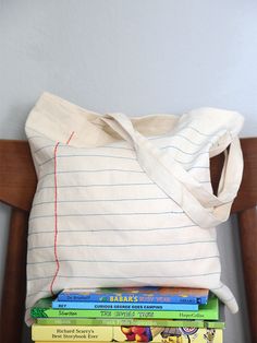 a stack of books sitting on top of a wooden chair next to a white bag