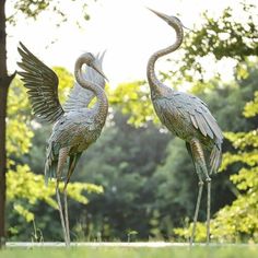 two metal birds standing next to each other on top of a grass covered field with trees in the background