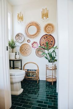 a white toilet sitting in a bathroom next to a green tiled floor and wall with decorative plates on it