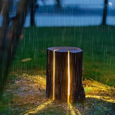 a tree stump that has been turned into a lamp in the rain with its light shining on it