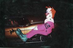 a clown sitting on the hood of a car