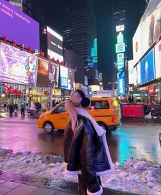 a woman standing in the middle of a busy city street at night with traffic and billboards