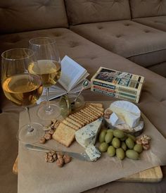 two glasses of wine, cheese and crackers sit on a table next to a couch