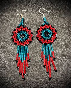 red, blue and black beaded earrings with fringes on top of leather surface