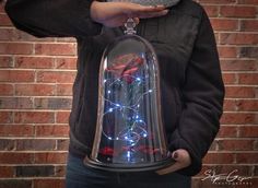 a woman is holding a bell jar with roses in it and lights on the inside