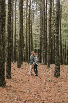 an engaged couple standing in the middle of a forest with their arms around each other