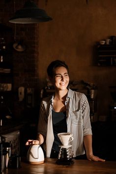 a woman sitting at a table with a coffee pot in front of her, smiling