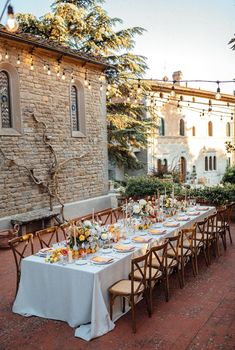 a long table is set up outside in front of a stone building with string lights