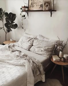 a bed with white sheets and pillows next to a potted plant on a table