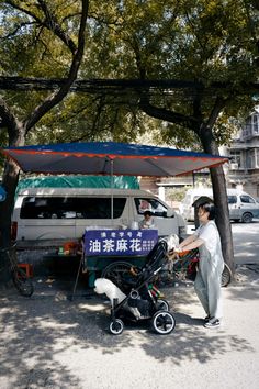 a woman standing next to a baby stroller under an umbrella on the side of a road