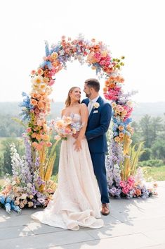 a bride and groom standing in front of a colorful floral arch