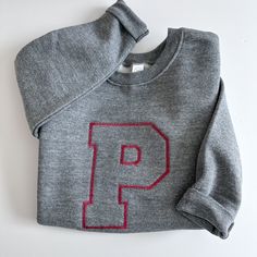 Choose from heather grey, granite, navy, pink, black or royal. Each sweatshirt is made from 60% cotton and 40% polyester. Each sweatshirt is embroidered with a large outline varsity letter.  Please wash on cold and dry on low. If you are wanting a different design, more wording, or a different clothing style, please send me a message so we can discuss the details. In the notes to seller please enter the name/wording exactly how you would like it to read Sporty Sweater With Letter Embroidery For Winter, Sporty Winter Sweater With Letter Embroidery, Fall Tops With School Spirit Letter Embroidery, Gray Crew Neck Sweater With Embroidered Logo, College Gray Sweatshirt With Embroidered Logo, Fall School Tops With Embroidered Logo, Long Sleeve Sweatshirt With Embroidered Logo For School, Gray Embroidered Logo Sweatshirt For Winter, Gray Embroidered Logo Sweatshirt For Fall