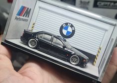 a hand holding up a black toy car in front of a bmw garage door with the logo on it