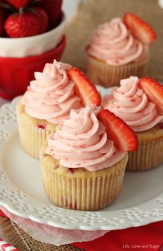 three cupcakes with pink frosting and strawberries on the top are sitting on a white plate