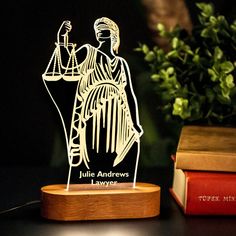 a lady justice statue on top of a table next to some books and a plant