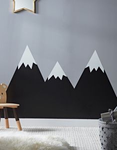 a teddy bear sitting on a stool in front of a wall with mountains painted on it