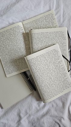 three open notebooks sitting on top of each other next to a pair of glasses