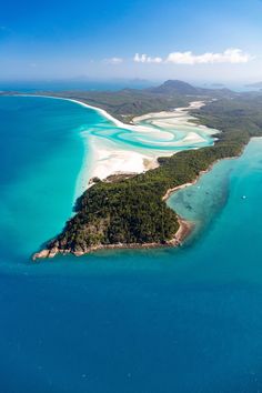 an island in the middle of blue water with white sand and trees on it's sides