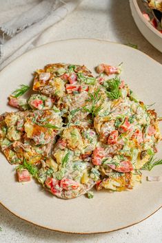 a white plate topped with potato salad next to a bowl of potatoes and carrots