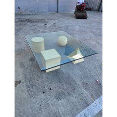 a glass table sitting on top of a cement ground next to a bag and an object