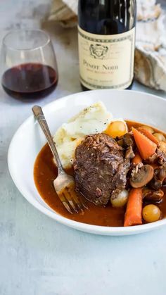 a white plate topped with meat and veggies next to a bottle of wine