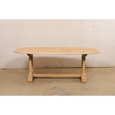 an oval wooden table sitting on top of a cement floor next to a white wall