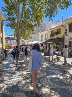 people are walking down the street in front of shops and buildings on a sunny day