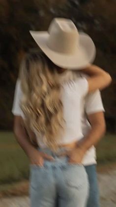 two people standing next to each other in front of trees and grass, one wearing a white cowboy hat