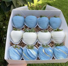 a box filled with blue and white chocolate covered strawberries next to green leaves on top of grass