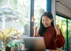 a woman sitting at a table in front of a laptop computer and raising her fist