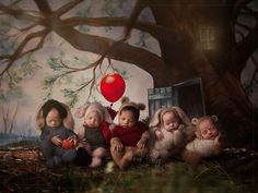 a group of babies sitting next to each other in front of a tree with red balloons