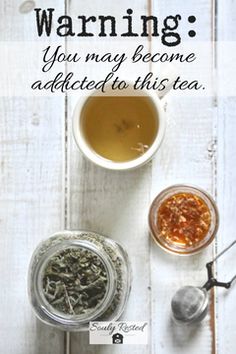 a cup of tea next to two jars filled with different types of teas on top of a white wooden table