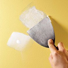 someone using a spatula to paint a wall with yellow and white paint on it