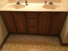 two sinks in a bathroom with brown cabinets and tile on the floor next to each other