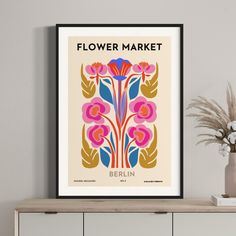 a flower market poster hangs on the wall next to a vase with flowers in it