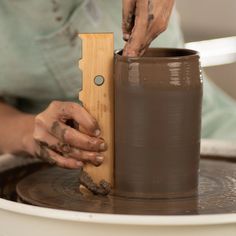 a person making a vase out of clay on a potter's wheel with a wooden block