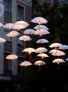 many white umbrellas are hanging in front of a tall building at night with lights on them